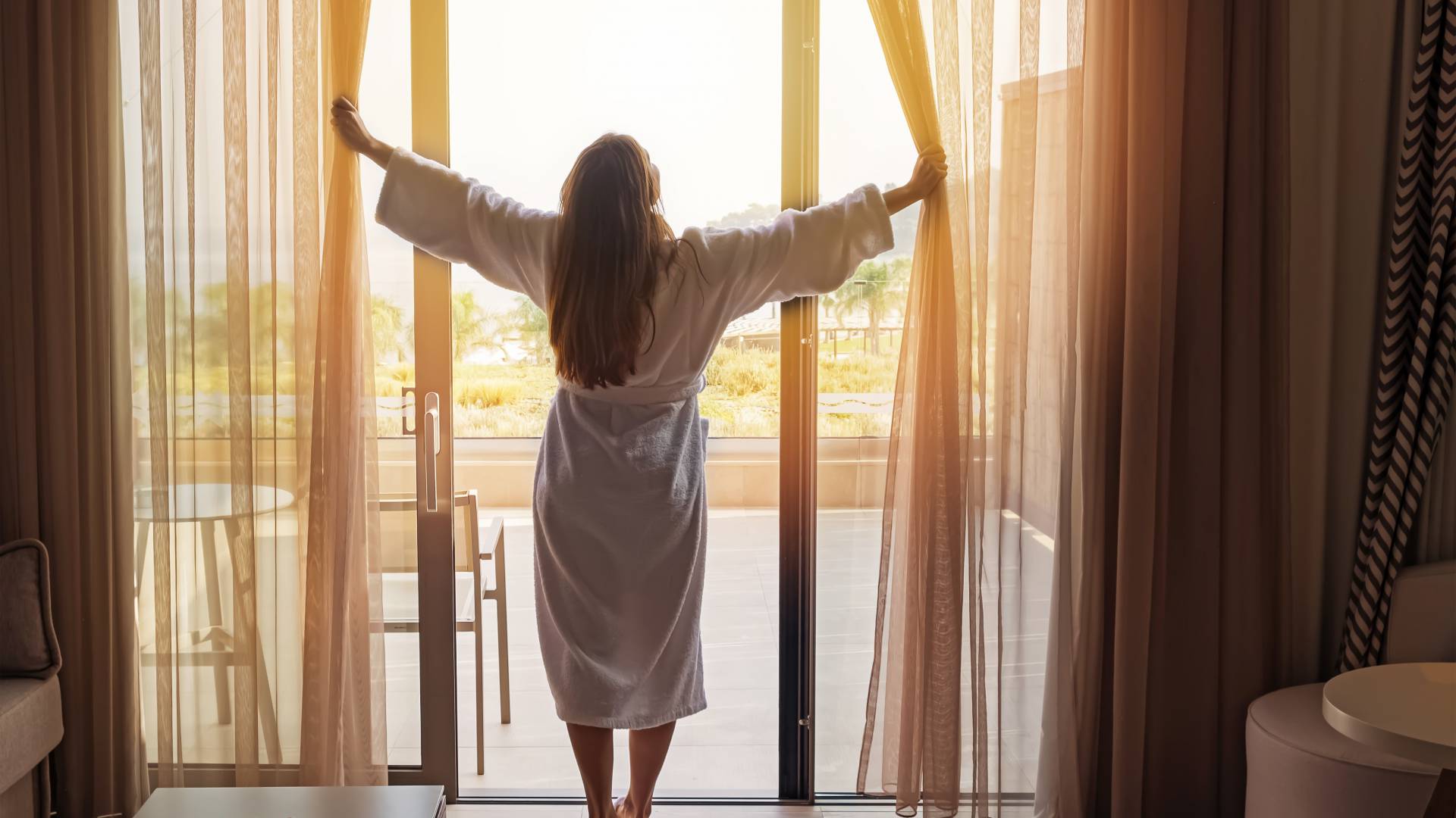 Frau öffnet morgens die Vorhänge im Hotelzimmer