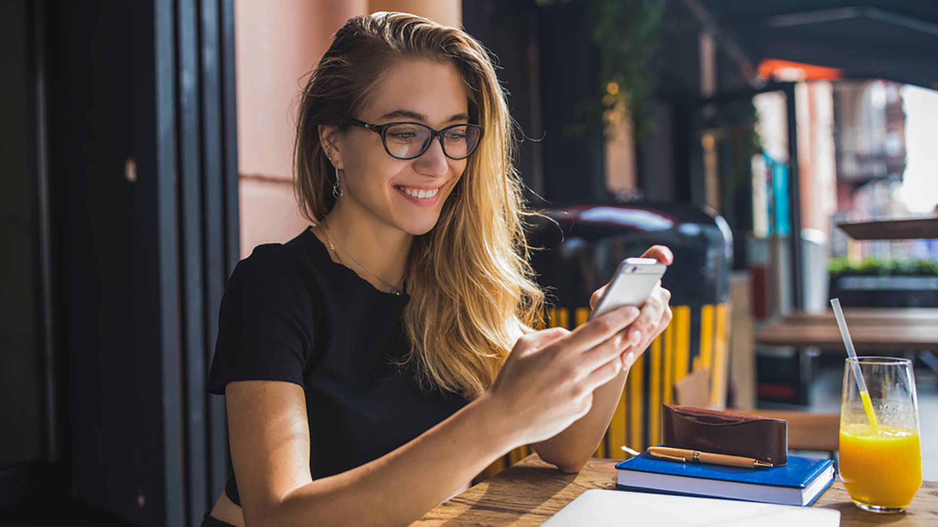 Frau mit Brille beim Saft trinken in einer Bar mit Handy in der Hand