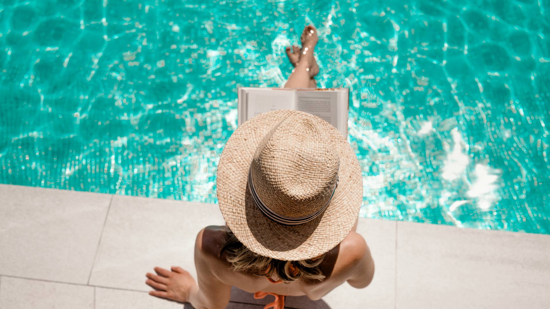 Frau sitzt am Pool und liest ein Buch