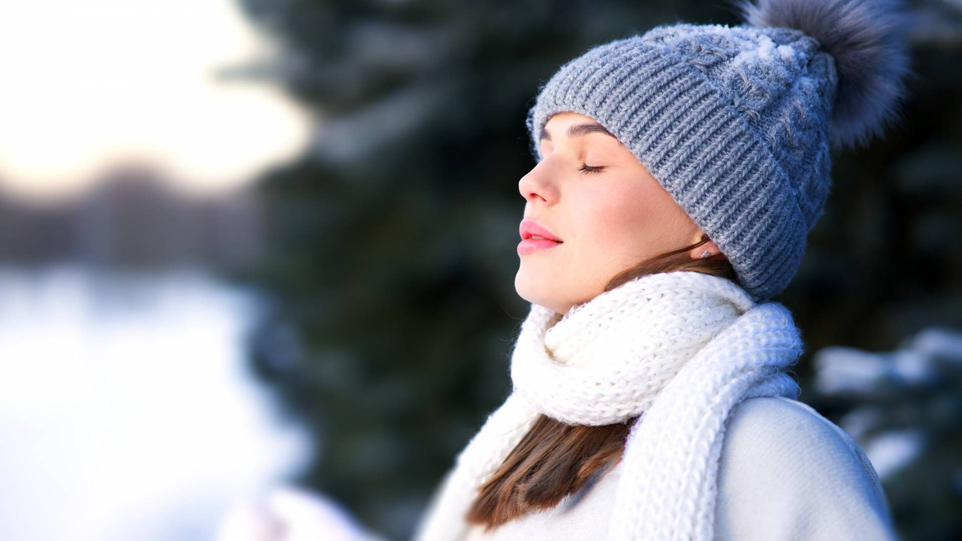 Woman in a hat and scarf stands in the fresh air in winter and takes a deep breath.