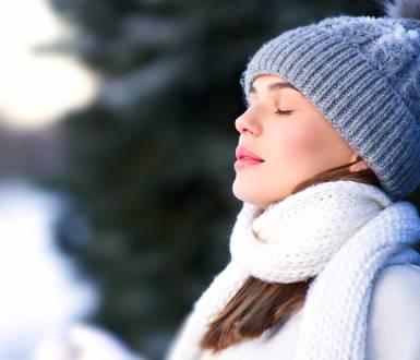 Woman in a hat and scarf stands in the fresh air in winter and takes a deep breath.
