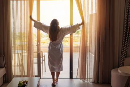 Frau öffnet morgens die Vorhänge im Hotelzimmer