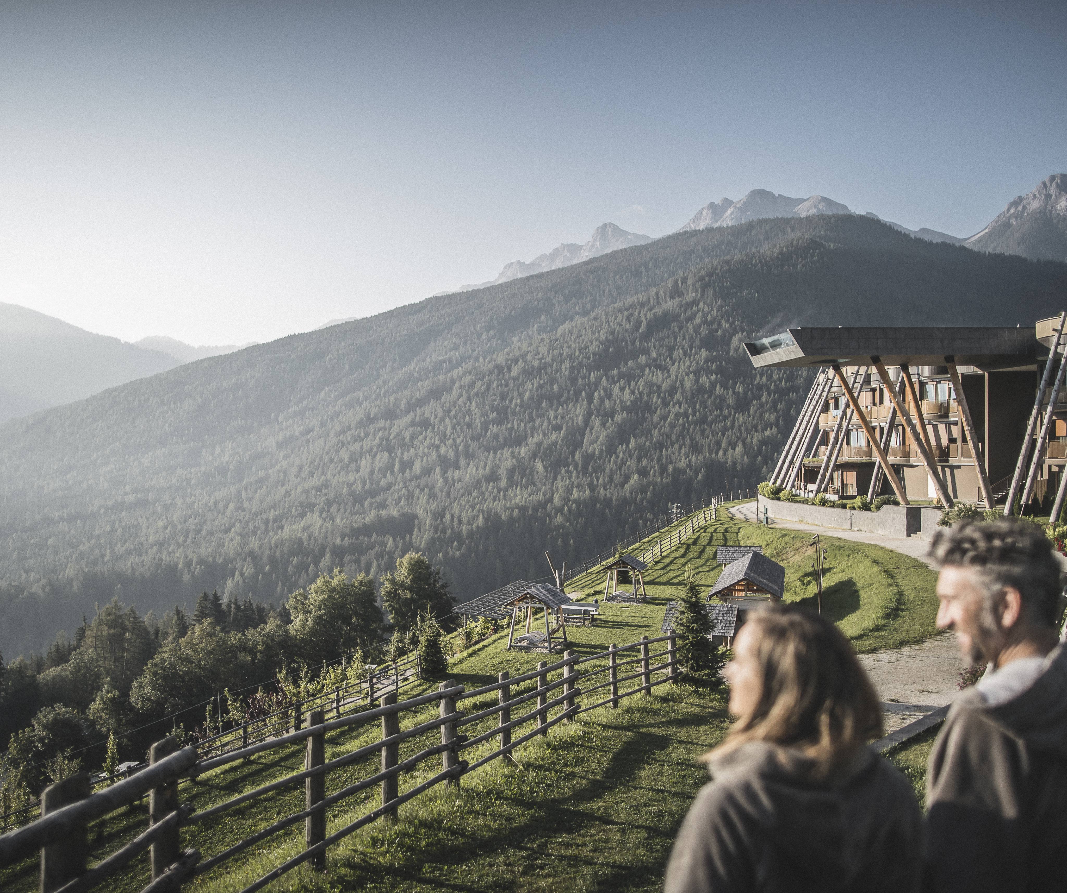 Paar blickt auf die umliegenden Berge. Dahinter ein hotel mit Infinity-Sky-Pool